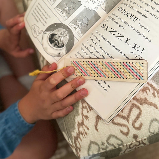Person holding a colorful bookmark over a book with text and illustrations.