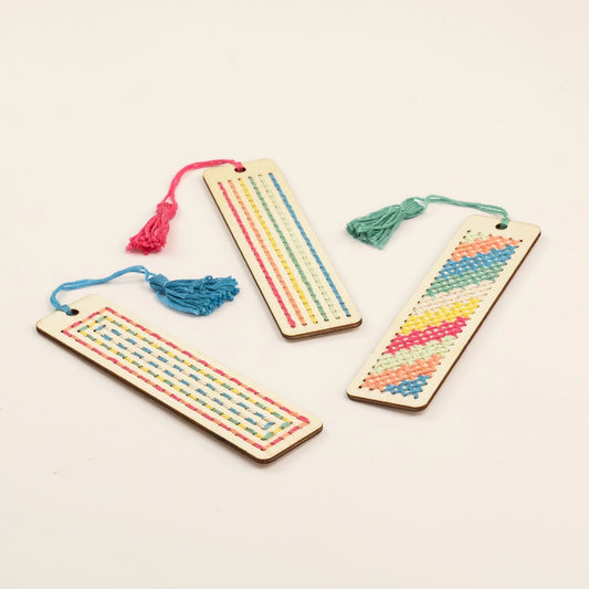 Three wooden bookmarks with colorful thread patterns on a light beige background