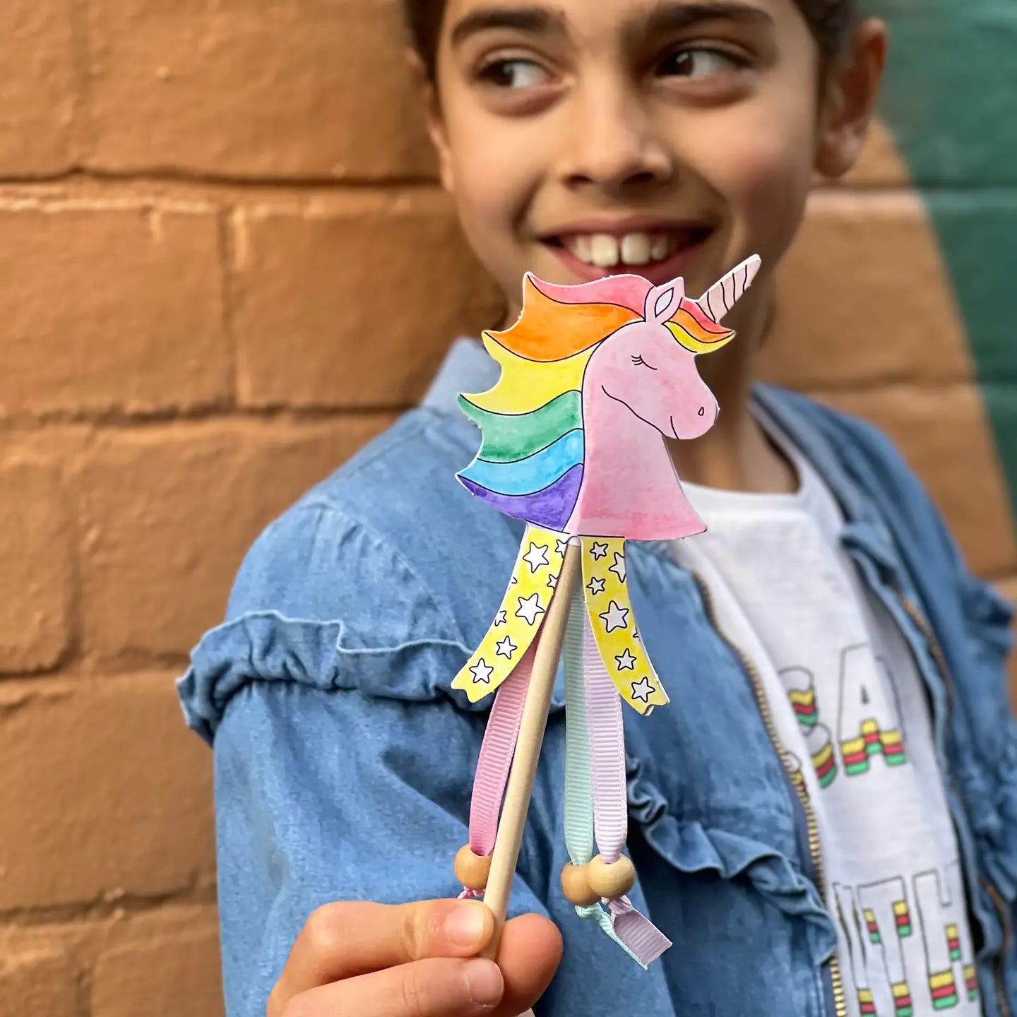 Child holding a colorful unicorn toy against a brick wall.