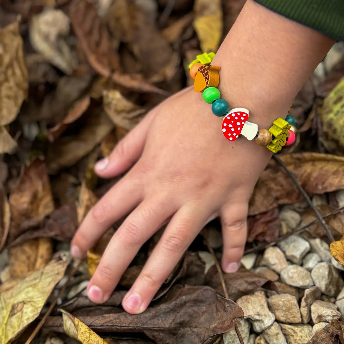 Child's hand wearing a colorful beaded bracelet on a leafy ground