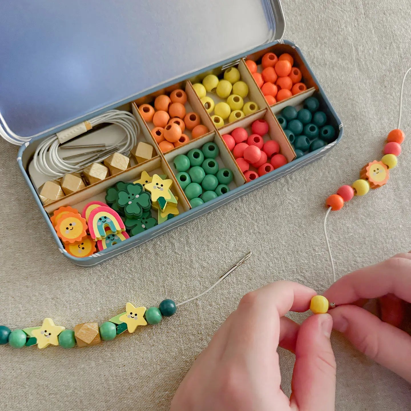 Colorful bead set in a tin with hands stringing beads on a thread.