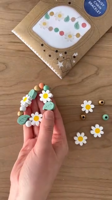 Decorative flower-shaped clips held by a hand on a wooden surface with additional clips and a decorative box in the background.